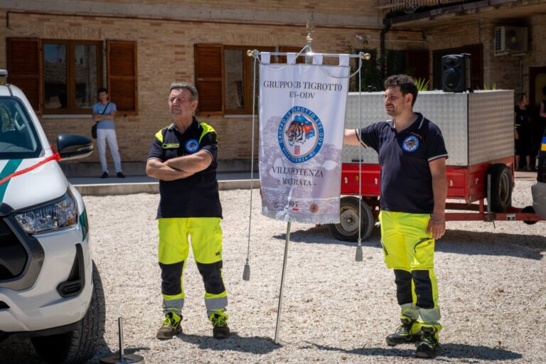 Due volontari accanto al gagliardetto del Gruppo CB Tigrotto, con il pickup a sinistra e la motopompa carrellata sullo sfondo