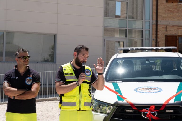 Il presidente dell'associazione parla al microfono davanti al pickup con il fiocco rosso