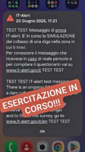 Schermata di un telefono con la notifica IT-alert del 20 giugno 2026 alle 11:21 che annuncia la simulazione del collasso di una diga