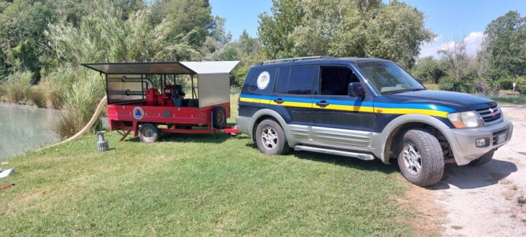 Il fuoristrada attaccato al carrello rosso della motopompa, su un prato accanto al fiume