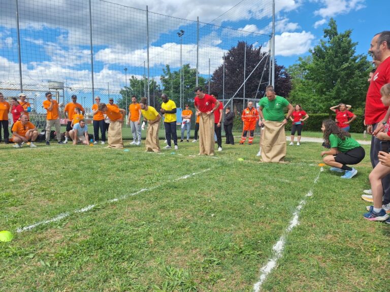 Quattro concorrenti dentro i sacchi di juta pronti a partire sul campo erboso, con il pubblico delle contrade ai lati
