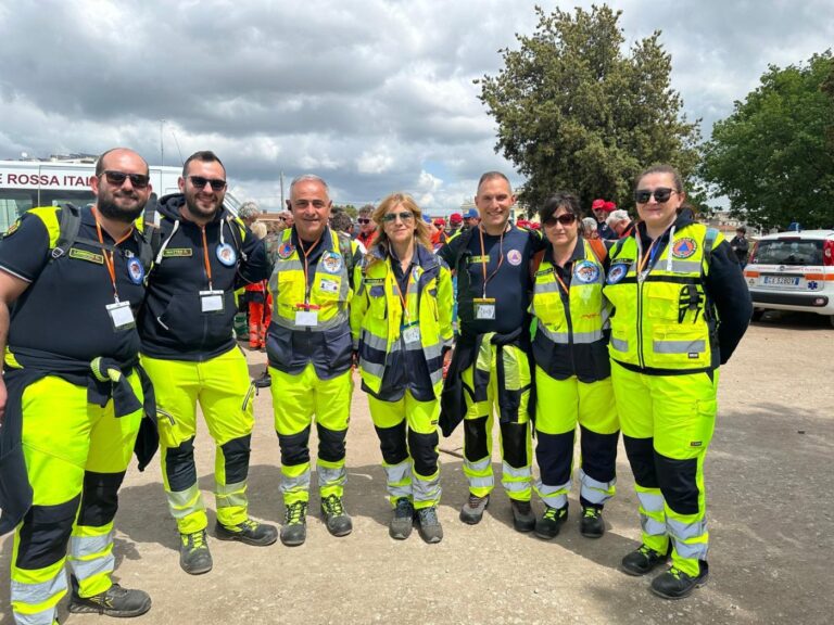 Sette volontari del gruppo al campo base, con i mezzi della Croce Rossa alle spalle