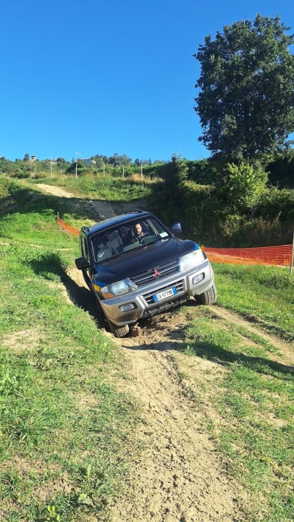 Il Pajero visto di tre quarti mentre affronta una salita di terra battuta al crossodromo, con il cielo azzurro e la rete arancione del tracciato sullo sfondo