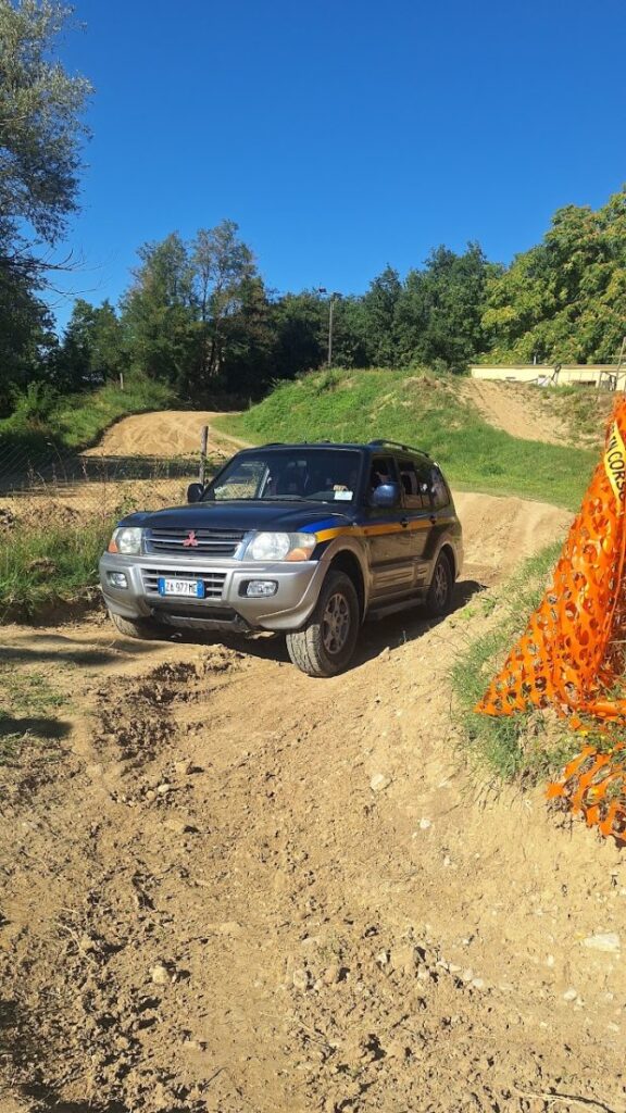 Il Pajero fermo su uno sterrato in discesa, delimitato da una rete arancione da cantiere, in mezzo alla campagna