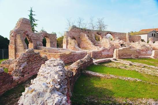 I muri in laterizio dell'area archeologica di Helvia Recina con la vegetazione intorno e le case della frazione sullo sfondo