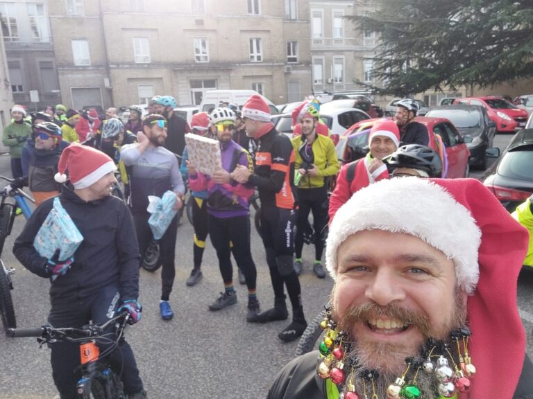 Sul piazzale dell'ospedale i partecipanti aspettano con i pacchi regalo incartati in mano; in primo piano un partecipante con le palline di Natale appese alla barba