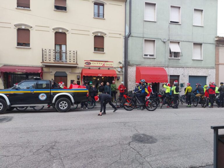 Il pickup blu e giallo del Gruppo CB Tigrotto fermo davanti al Caffè x Caso di Villa Potenza con un grande pacco regalo sul cassone; accanto, i partecipanti con le biciclette in attesa della partenza