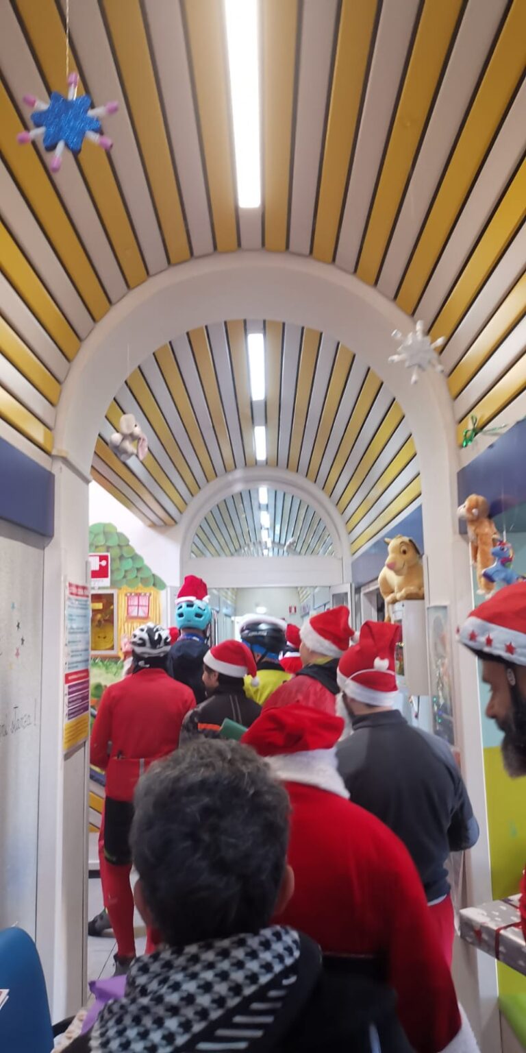 La fila dei partecipanti attraversa il corridoio del reparto di pediatria, sotto il soffitto a strisce gialle e blu e fra i disegni colorati alle pareti