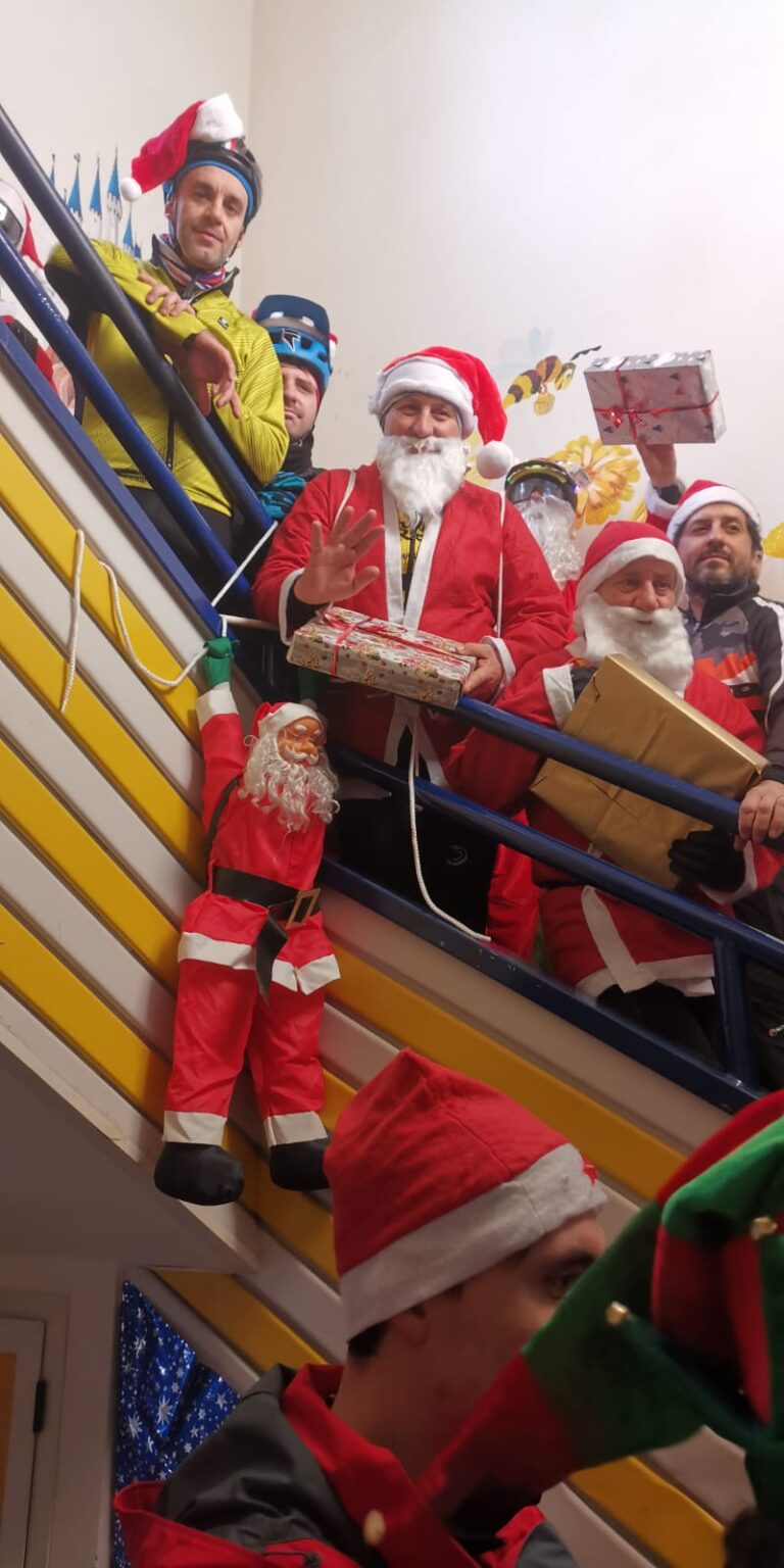 Alcuni partecipanti vestiti da Babbo Natale sulle scale del reparto, con i pacchi regalo in mano; alla ringhiera è appeso un pupazzo di Babbo Natale