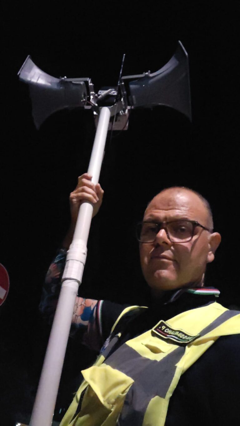 Di notte, un volontario del Gruppo CB Tigrotto con il gilet ad alta visibilità regge sopra la testa un'asta con in cima due grandi trombe di un altoparlante
