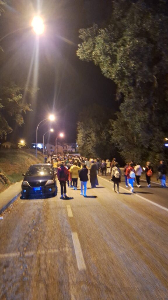 La strada illuminata dai lampioni con centinaia di persone che camminano in fila verso il convento